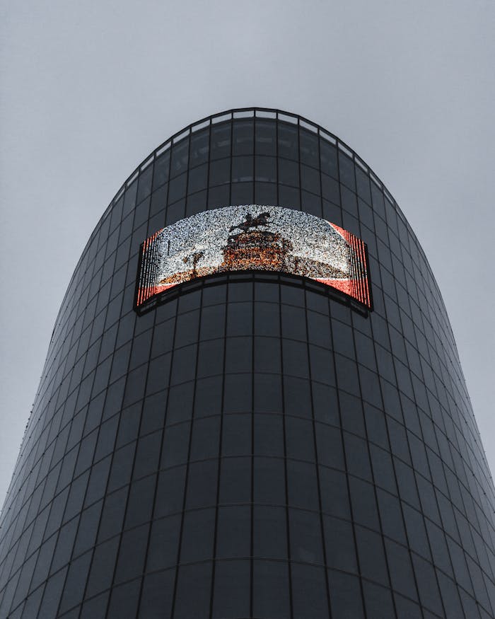 From below of modern building with glass walls and screen against cloudy gray sky in daylight